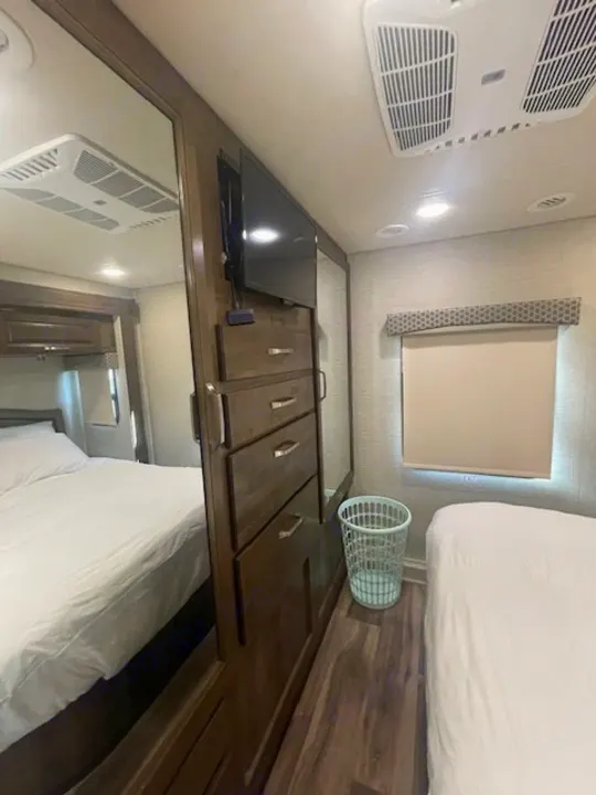 RV rental interior view of a bedroom with two beds, a mounted TV, and wooden storage cabinets.. Jayco Greyhawk 2019