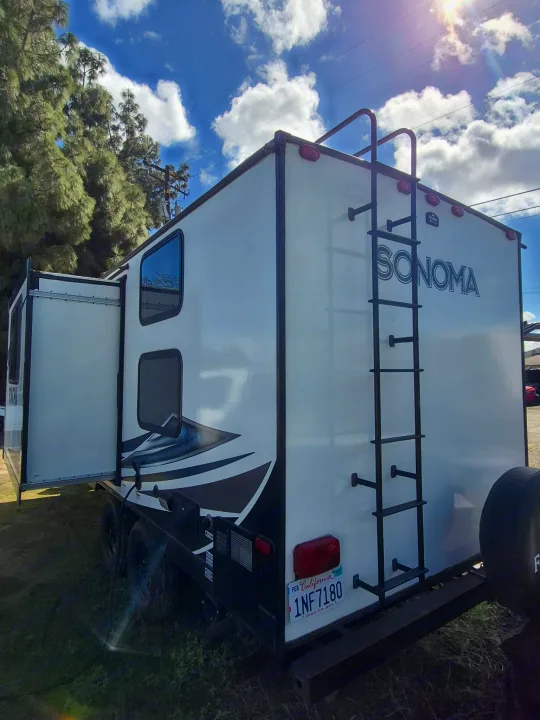 White Sonoma RV rental, a travel trailer with its slide-out open, parked on grass under a sunny, cloudy sky.. Forest River Sonoma 2020