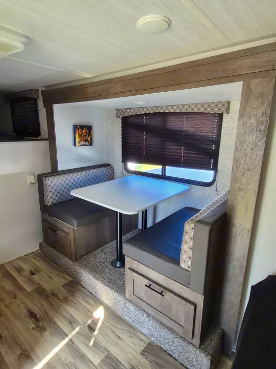 This **rv rental** interior features a cozy dinette area with a white table, upholstered storage benches, and a window with blinds.. Forest River Sonoma 2020