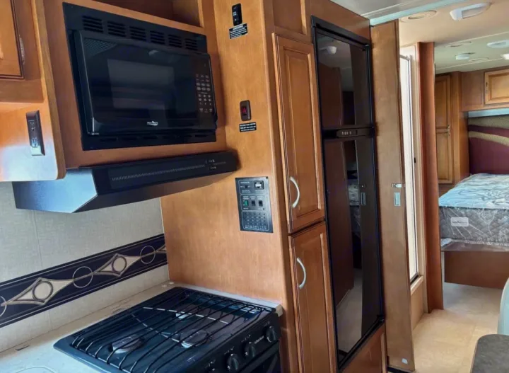 RV rental interior featuring a compact kitchen with a microwave, range hood, stovetop, and refrigerator, leading to a cozy bedroom.. Winnebago Minnie Winnie 2015