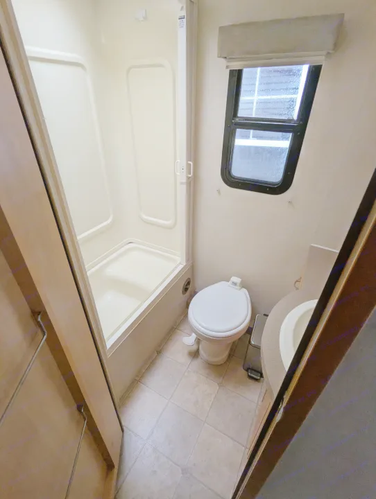 Compact RV rental bathroom: shower stall, toilet, and sink area with a window and tiled floor.. Triple E Regency 2006
