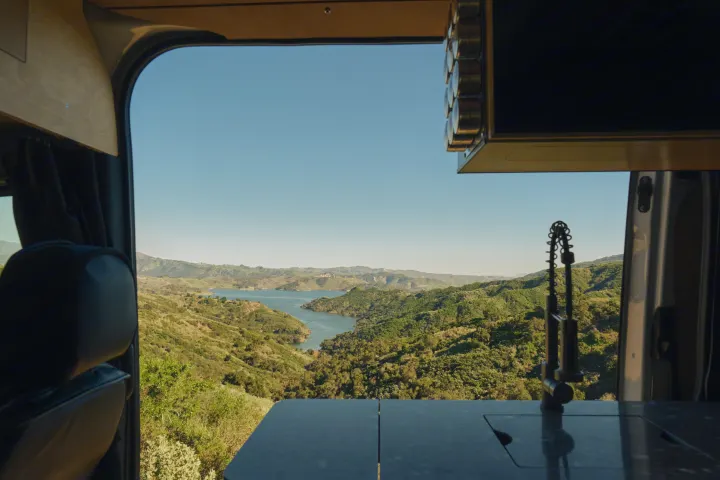 Scenic lake and green hills from an RV rental van, showing an interior counter and faucet.. Mercedes Sprinter 2022