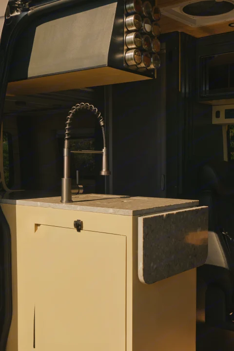 Inside an RV rental: a modern kitchen with a pull-down faucet, magnetic spice rack with various spices, and a light speckled countertop.. Mercedes Sprinter 2022