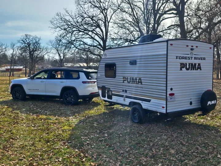 White Jeep Grand Cherokee L towing a Forest River Puma travel trailer. Ideal for your next RV rental adventure.. Palomino Puma Camping Edition 122BHCE 2026