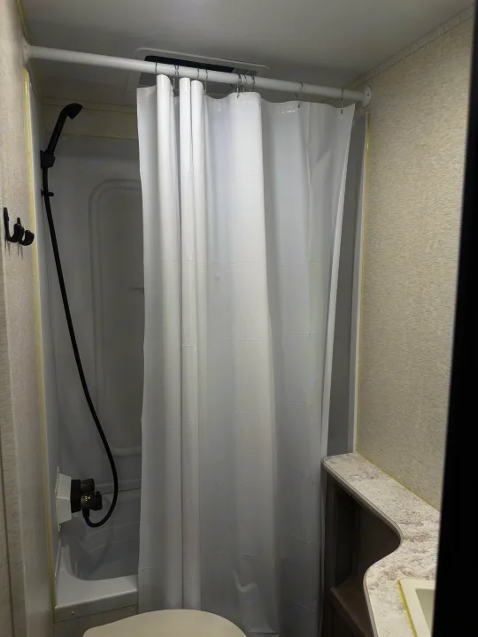 This RV rental's compact bathroom includes a shower with black fixtures, white curtain, toilet, and sink.. Crossroads RV Sunset Trail Sport 2025
