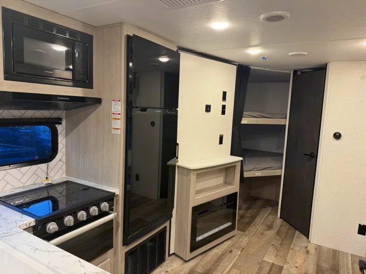 Spacious RV rental interior featuring a full kitchen with modern appliances, bunk beds, and a cozy electric fireplace.. Crossroads RV Sunset Trail Sport 2025