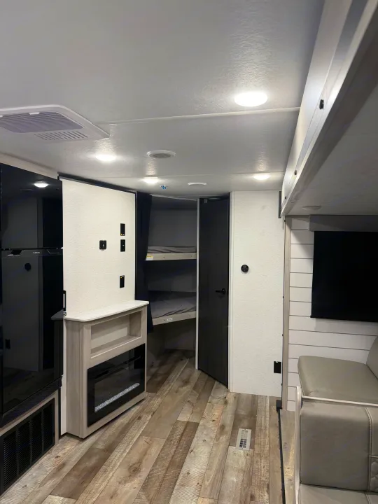 Modern RV rental interior with bunk beds, refrigerator, fireplace, and sofa. Bright, spacious living area.. Crossroads RV Sunset Trail Sport 2025