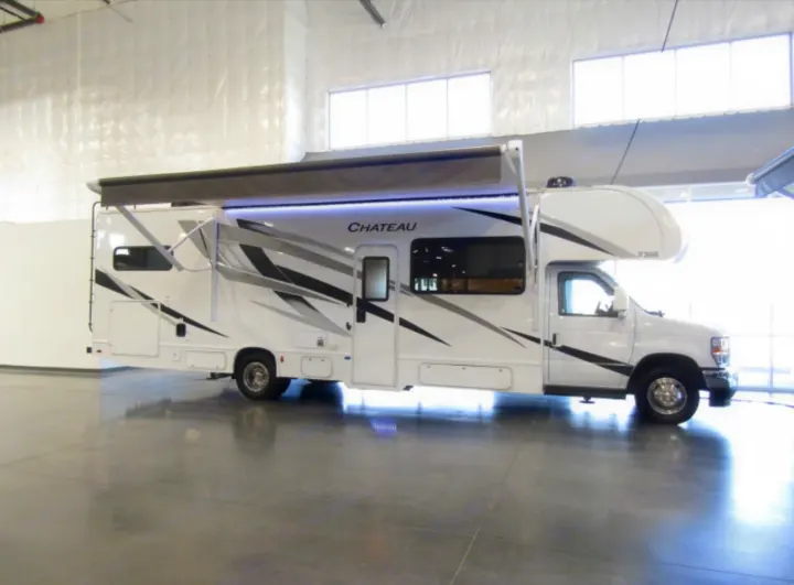 White Chateau Class C RV rental with an extended awning and LED lighting, parked indoors.. Thor Chateau 2024