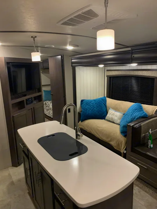 Modern RV rental interior featuring a kitchen island, cozy living area with sofa, and entertainment center.. Crossroads RV Sunset Trail Super Lite 2018