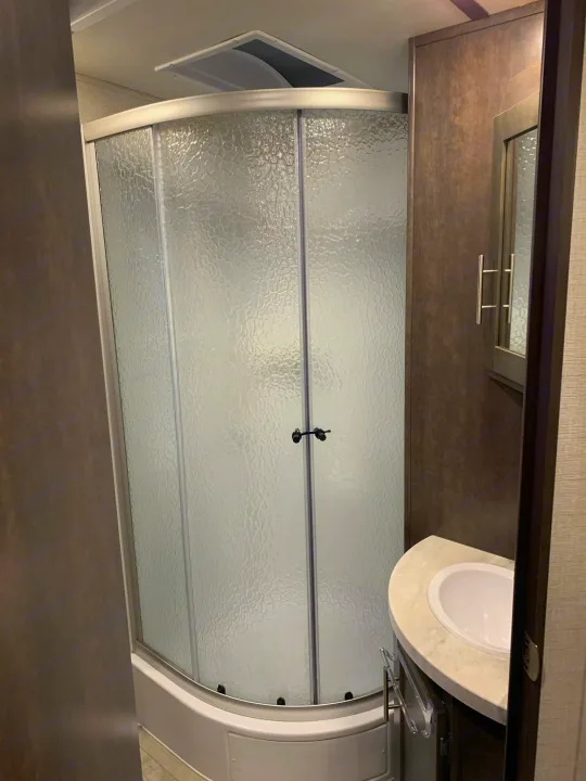 Inside an RV rental bathroom: a compact curved shower with frosted glass and a small vanity with a sink.. Crossroads RV Sunset Trail Super Lite 2018