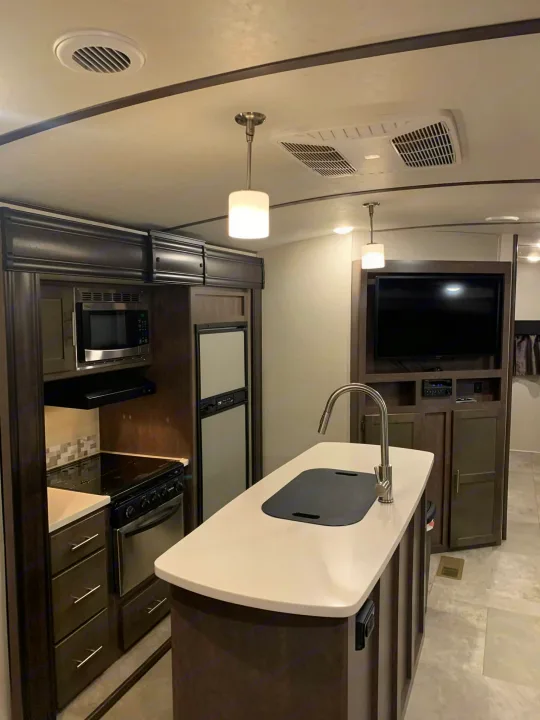 Modern RV rental kitchen interior featuring dark cabinets, stainless appliances, island with sink, and a TV.. Crossroads RV Sunset Trail Super Lite 2018