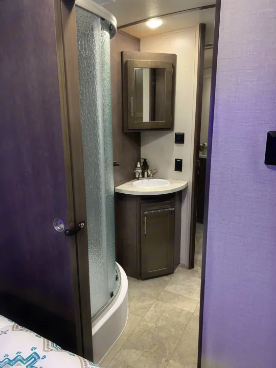 Inside an RV rental: a modern, compact bathroom with a corner sink, mirrored cabinet, and textured glass shower stall.. Crossroads RV Sunset Trail Super Lite 2018