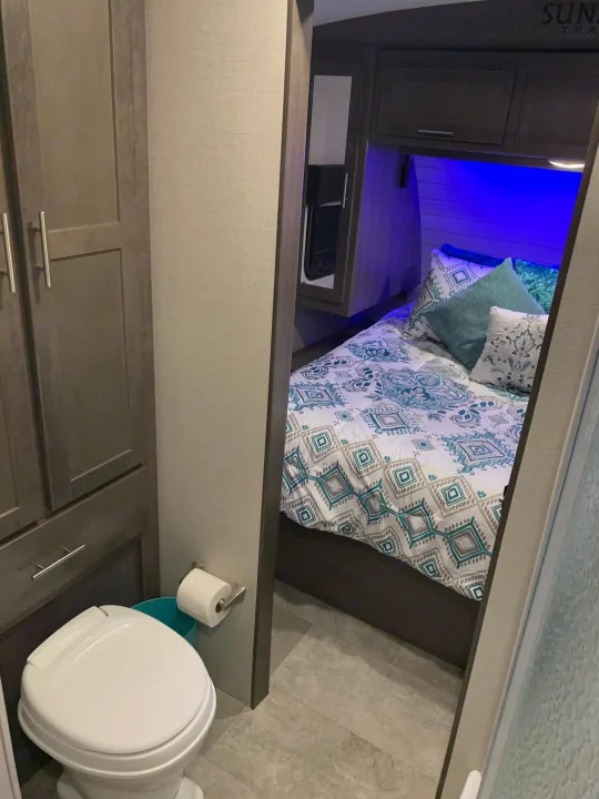 RV rental: Inside a compact RV showing the bedroom with patterned bedding & blue lights, and a small bathroom with a toilet.. Crossroads RV Sunset Trail Super Lite 2018