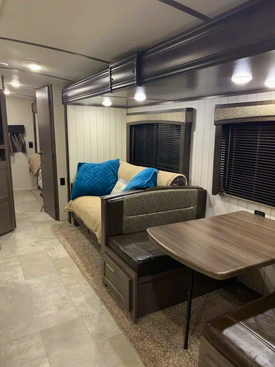 Cozy RV rental interior featuring a sofa with blue pillows, a dinette, and modern dark wood accents throughout the living space.. Crossroads RV Sunset Trail Super Lite 2018