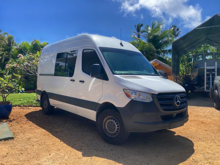 White Mercedes-Benz Sprinter RV rental parked on gravel in a sunny, tropical setting with palm trees and a blue sky.. Mercedes-Benz Sprinter 2020