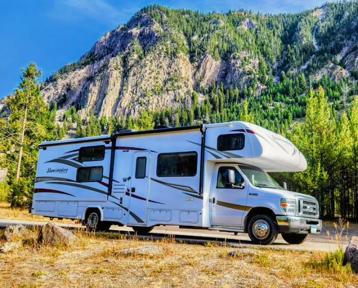 White Sunseeker rv rental motorhome parked on a road, fronting a majestic tree-covered mountain. Scenic nature adventure!. Forest River Sunseeker 2017