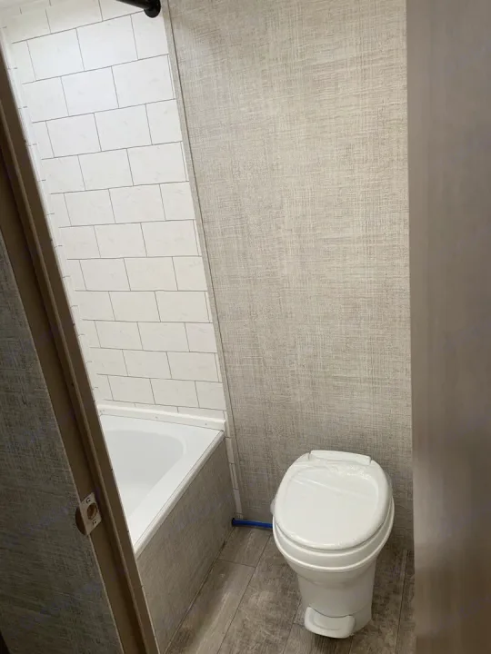 Inside an RV rental: a compact bathroom with white subway tile shower, tub, and toilet. Textured walls and wood-look floor.. Gulf Stream Ameri-Lite Super Lite 2022