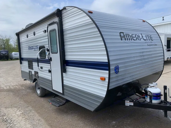 An Ameri-Lite Super-Lite travel trailer, grey with blue stripe, featuring an awning and propane tanks. Perfect rv rental.. Gulf Stream Ameri-Lite Super Lite 2022