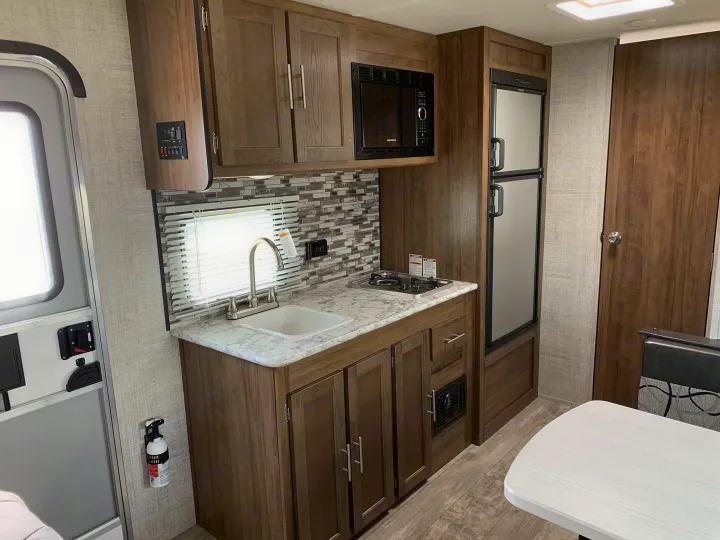 This RV rental kitchen features a sink, stovetop, microwave, refrigerator, and wood-grain cabinetry, ready for travel.. Gulf Stream Ameri-Lite Super Lite 2022