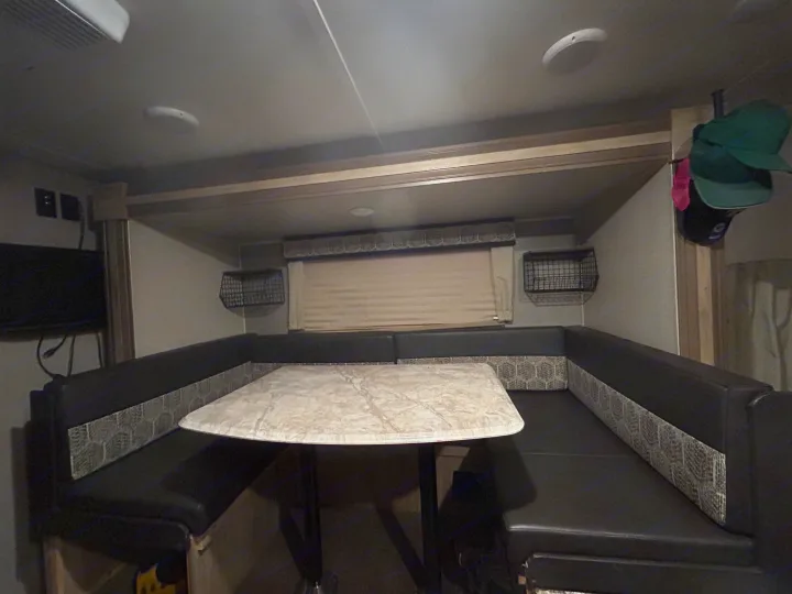 Cozy RV rental dinette with dark U-shaped booth seating, patterned backrests, and light-colored table for meals.. Coachmen Catalina Summit 2021