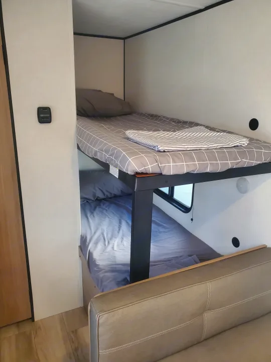 Cozy bunk beds in an RV rental, providing a practical sleeping area. Features light walls, thermostat, and comfortable bedding.. Keystone Coleman 2026