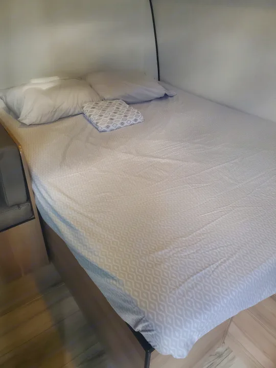 Cozy RV rental bed with light patterned sheets and pillows, offering a comfortable sleeping area inside for travelers.. Keystone Coleman 2026