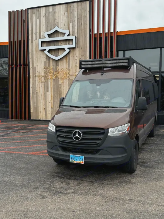 Brown Mercedes-Benz Sprinter rv rental van with a roof light bar, parked outside a Harley-Davidson Sturgis building.. Mercedes-Benz Sprinter 2023
