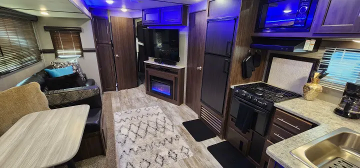 Modern rv rental interior: kitchen with stove/sink, living room with couch, TV, and electric fireplace. Blue lighting.. Crossroads RV Zinger 2019