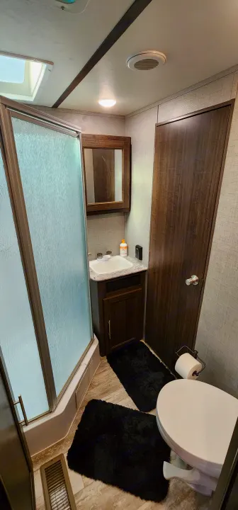 RV rental bathroom with textured glass shower, vanity sink, mirror, toilet, and dark wood accents. Includes overhead vent and light.. Crossroads RV Zinger 2019