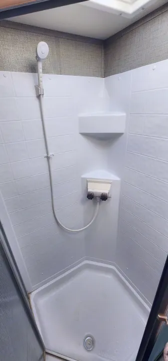 Compact white shower stall in an rv rental, with a handheld showerhead, corner shelf, and simple knob water controls.. Crossroads RV Zinger 2019