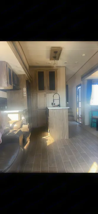 Modern RV rental interior: kitchen with light wood cabinets, black faucet, and living area featuring a dark sofa & wood-look tile floor.. Forest River Cherokee Arctic Wolf 2020