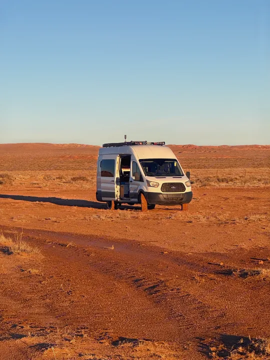 Adventure-ready rv rental van with open door, parked off-road in a wide desert with red earth under a clear sky.. Ford Van 2015