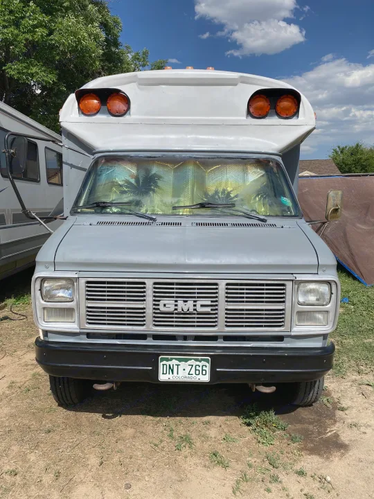 Gray GMC camper van RV rental with Colorado plate DNT-Z66 and palm tree sunshade. Frontal view of vintage RV.. GMC Vandura 1986