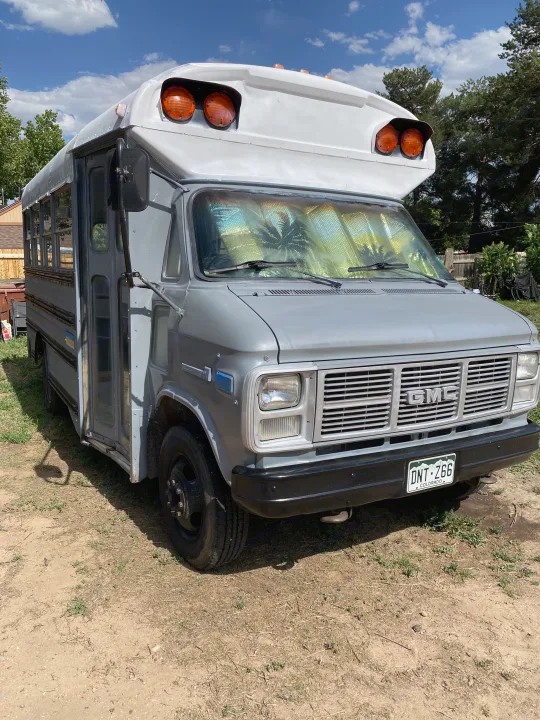 Gray GMC bus conversion for RV rental, with a palm tree reflection on the windshield under a blue sky.. GMC Vandura 1986