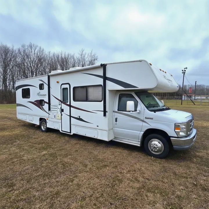 This white Class C motorhome rv rental is parked in a grassy field, ready for travel adventures on a cloudy day.. Coachmen Freelander 2011