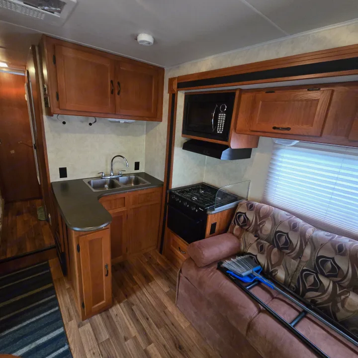 Bright RV rental interior features a full kitchen with sink, stove, microwave, and cozy sofa with patterned cushions.. Coachmen Freelander 2011