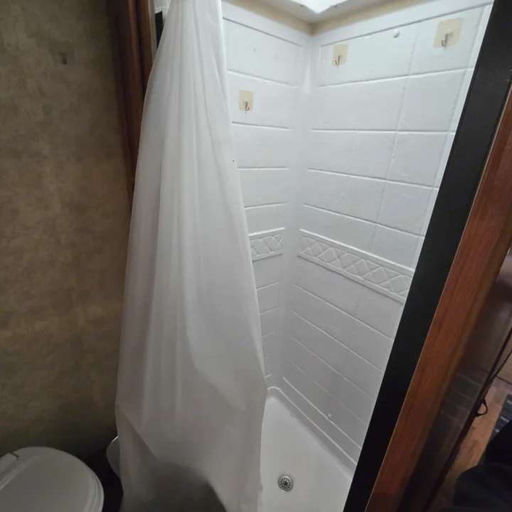 Compact shower and toilet in an RV rental bathroom, featuring white tiled walls and a shower curtain.. Coachmen Freelander 2011