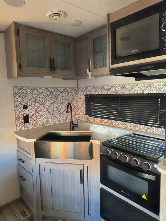 Inside an RV rental: a compact kitchen with a farmhouse sink, Greystone oven/stove, microwave & patterned backsplash.. Coleman Lantern 2022