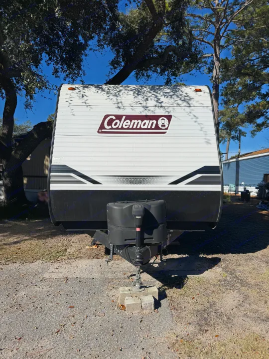 This Coleman travel trailer RV rental, ideal for camping adventures, is parked outdoors under trees on a sunny day.. Coleman Lantern 2022