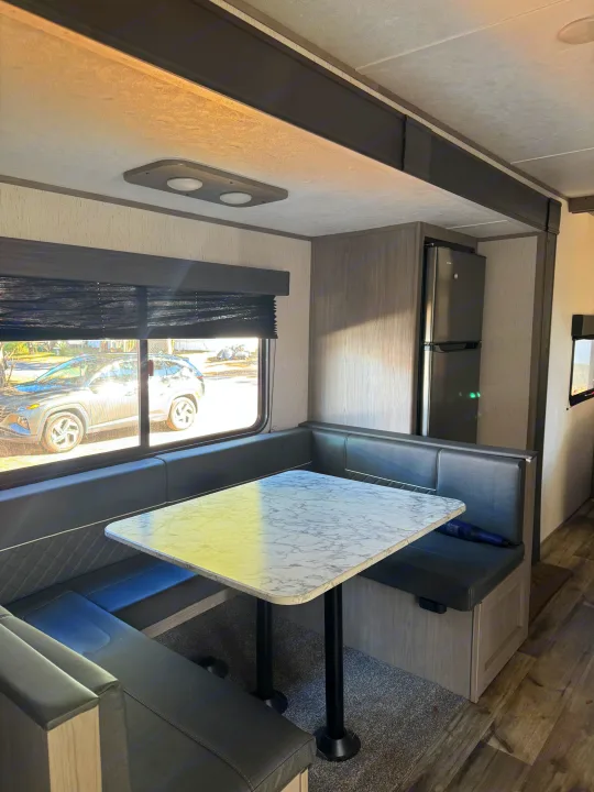 RV rental interior with a cozy booth dinette, marble-pattern table, and dark gray seating. A car is visible outside the window.. Coleman Lantern 2022