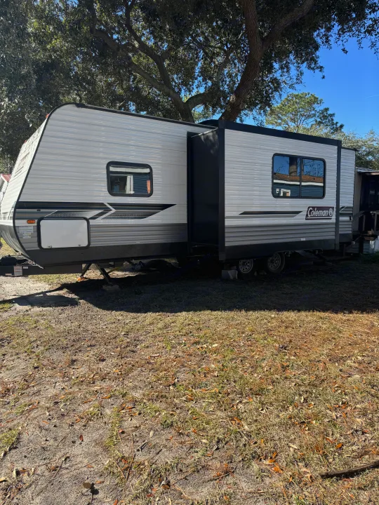 This Coleman travel trailer RV rental, with its slide-out extended, is parked on a sunny day in a grassy campground.. Coleman Lantern 2022