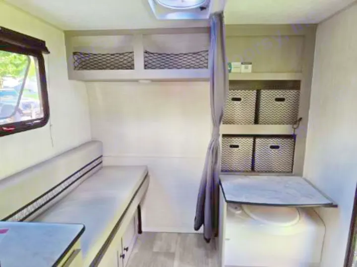 Cozy rv rental interior with compact bench seating/bed, overhead storage, and a bathroom featuring a composting toilet & baskets.. Clipper 3K 2025