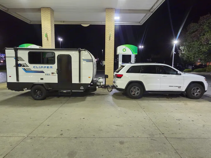 RV rental adventure: White Jeep Grand Cherokee towing a Clipper travel trailer at a brightly lit BP gas station at night.. Clipper 3K 2025