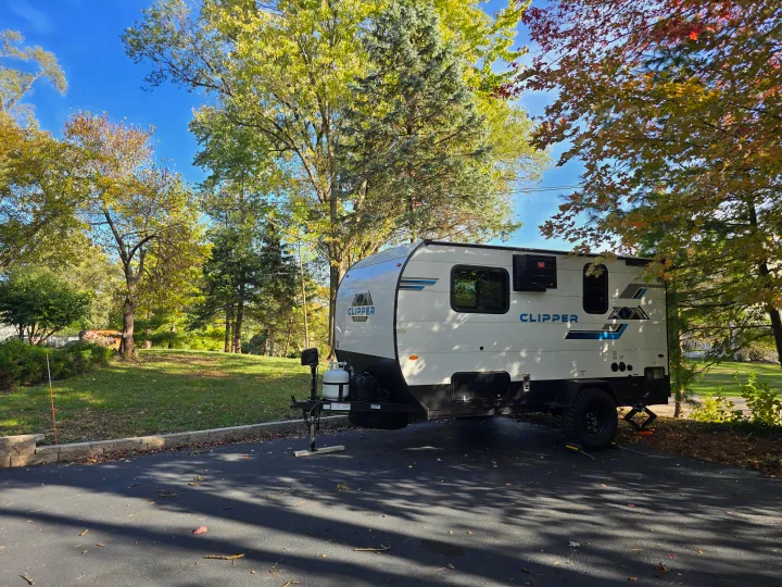 White Clipper travel trailer rv rental parked on asphalt, surrounded by bright autumn trees under a clear blue sky.. Clipper 3K 2025