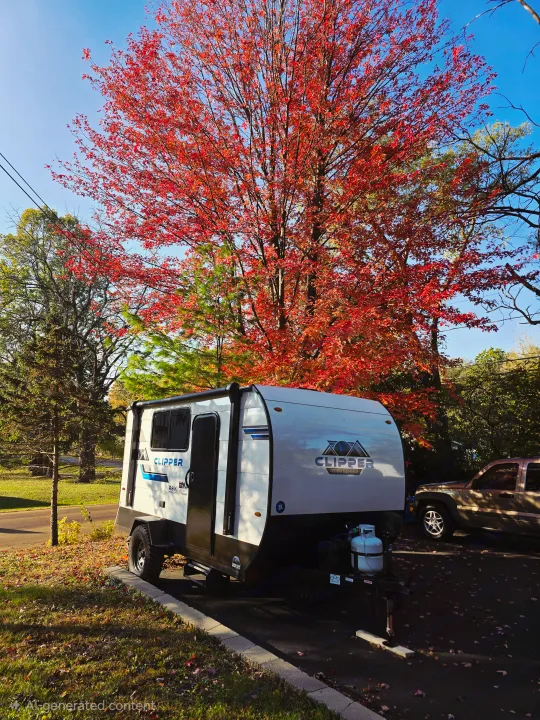 A white Clipper RV rental travel trailer is parked under a brilliant red maple tree, showcasing a vibrant autumn camping scene.. Clipper 3K 2025