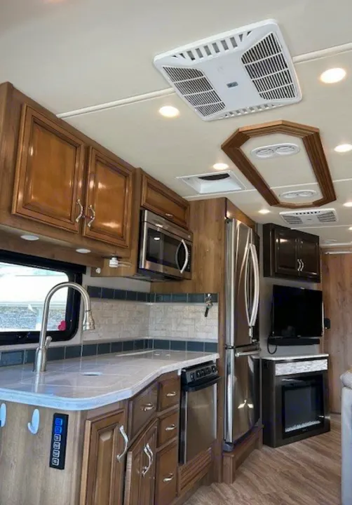 Modern RV rental kitchen and living area featuring stainless steel appliances, a cozy electric fireplace, and TV for your next adventure.. Bounder Bounder Motorhome 2019