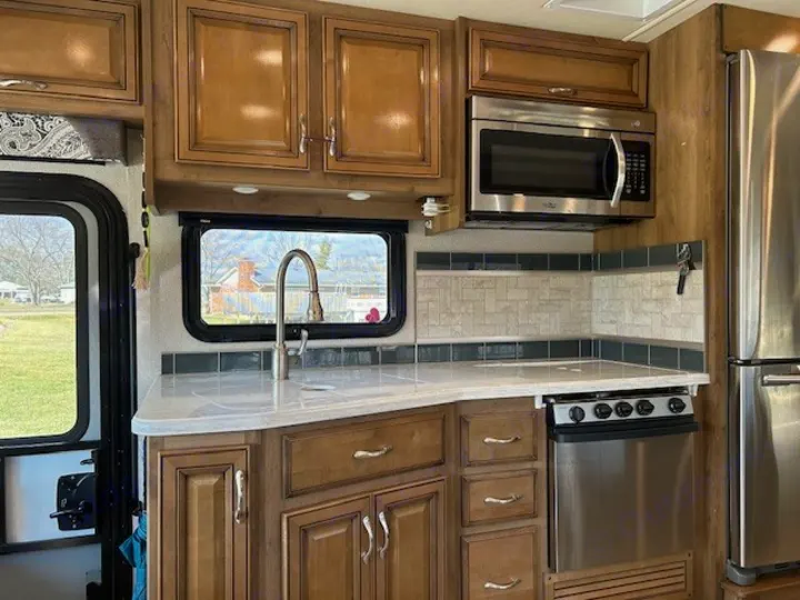 Spacious RV rental kitchen featuring a light counter, sink, wood cabinets, stainless microwave & fridge, and a tiled backsplash.. Bounder Bounder Motorhome 2019