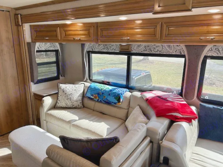 Cozy rv rental lounge with light sofas, patterned cushions, blankets, wooden cabinets, and an outdoor view.. Bounder Bounder Motorhome 2019