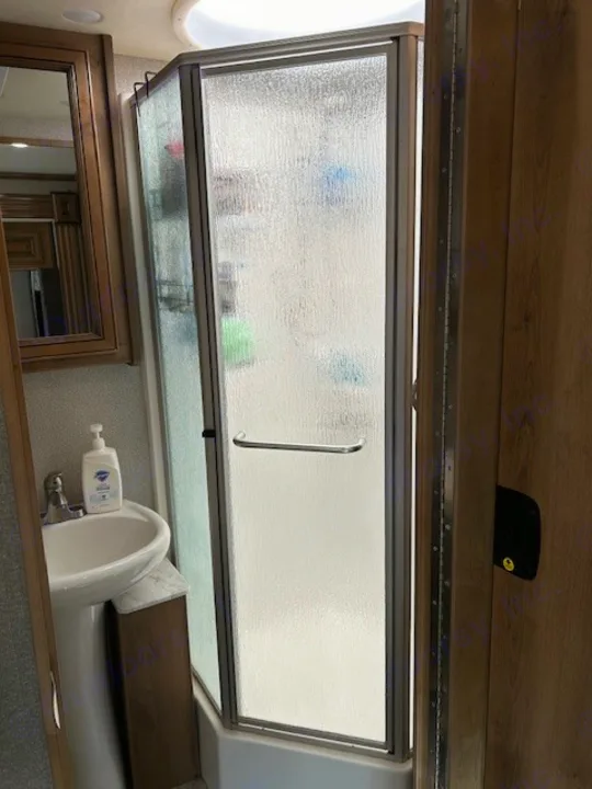 RV rental bathroom features a compact corner shower with frosted glass, sink with soap, and mirrored cabinet.. Bounder Bounder Motorhome 2019