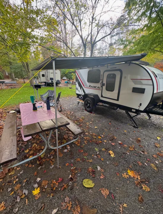 Cozy RV rental camping with a teardrop camper, picnic table, and autumn leaves on a gravel campsite under an awning.. Bontrager Outdoors 12RAD 2025